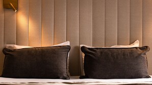 Habitación de hotel con cama, dos almohadas, luz empotrada en la pared y pared con textura.