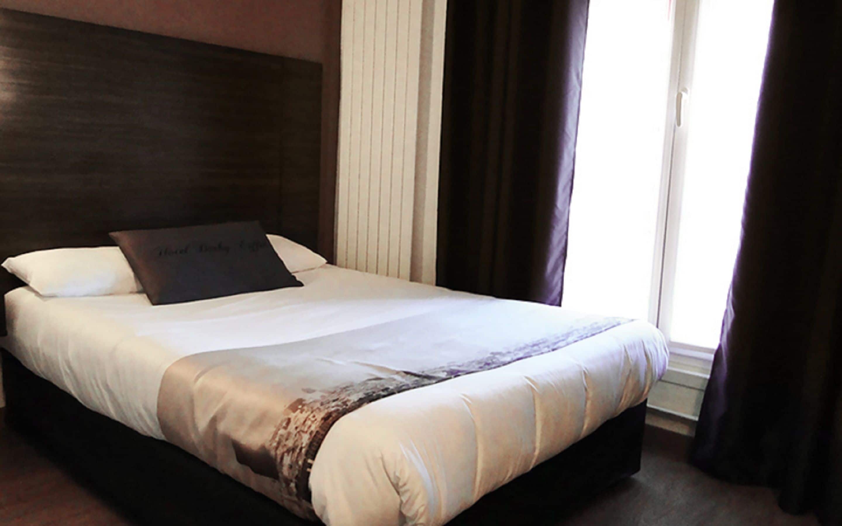 A neatly made bed with a dark headboard, white linens, and a decorative pillow.