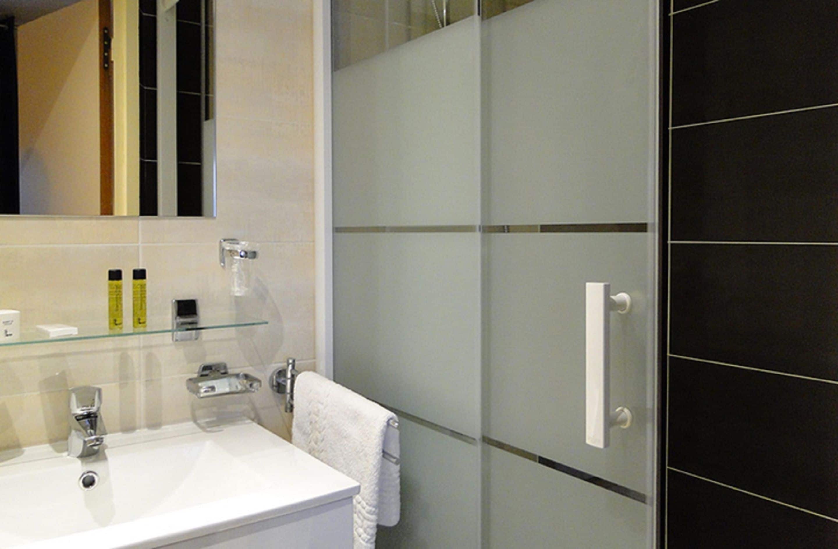 A modern bathroom with a glass shower enclosure, a white sink with a chrome faucet, and a towel hanging on a rack.