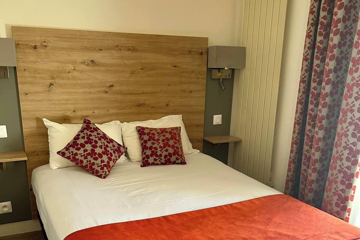 A neatly made bed with a red blanket, two pillows with a red and white pattern, and a wooden headboard.