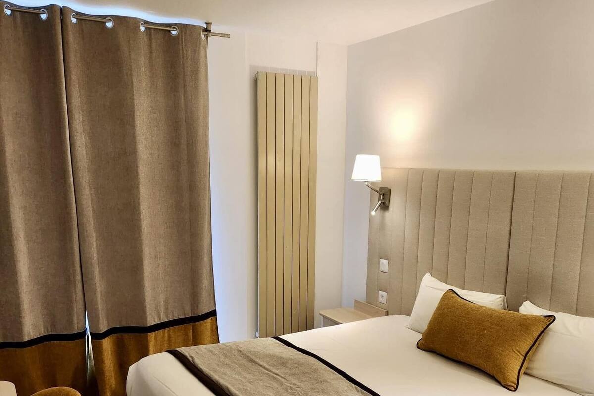 A hotel room with a large bed, a bedside table, a lamp, and curtains.