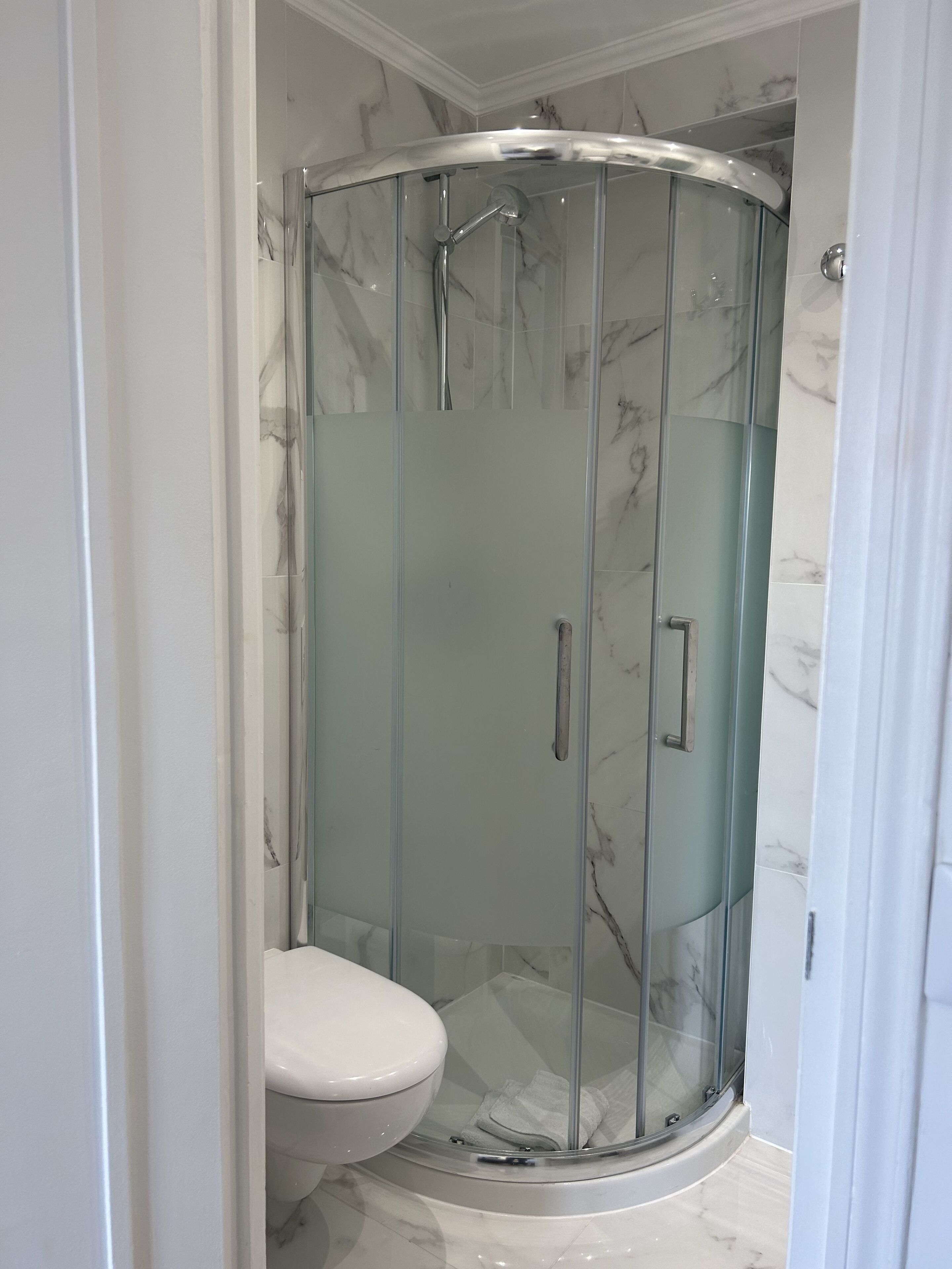 Ducha con paredes de mármol y diseño curvo, con inodoro en su interior.
