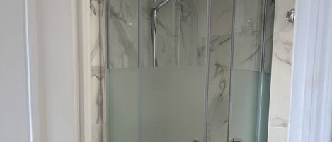 Ducha con paredes de mármol y diseño curvo, con inodoro en su interior.