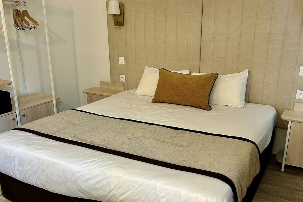 A hotel room with a large bed, a bedside table, a nightstand, and a wardrobe.