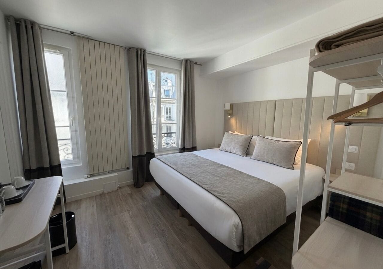 Quarto de hotel com cama, mesa de cabeceira e janela com cortinas.