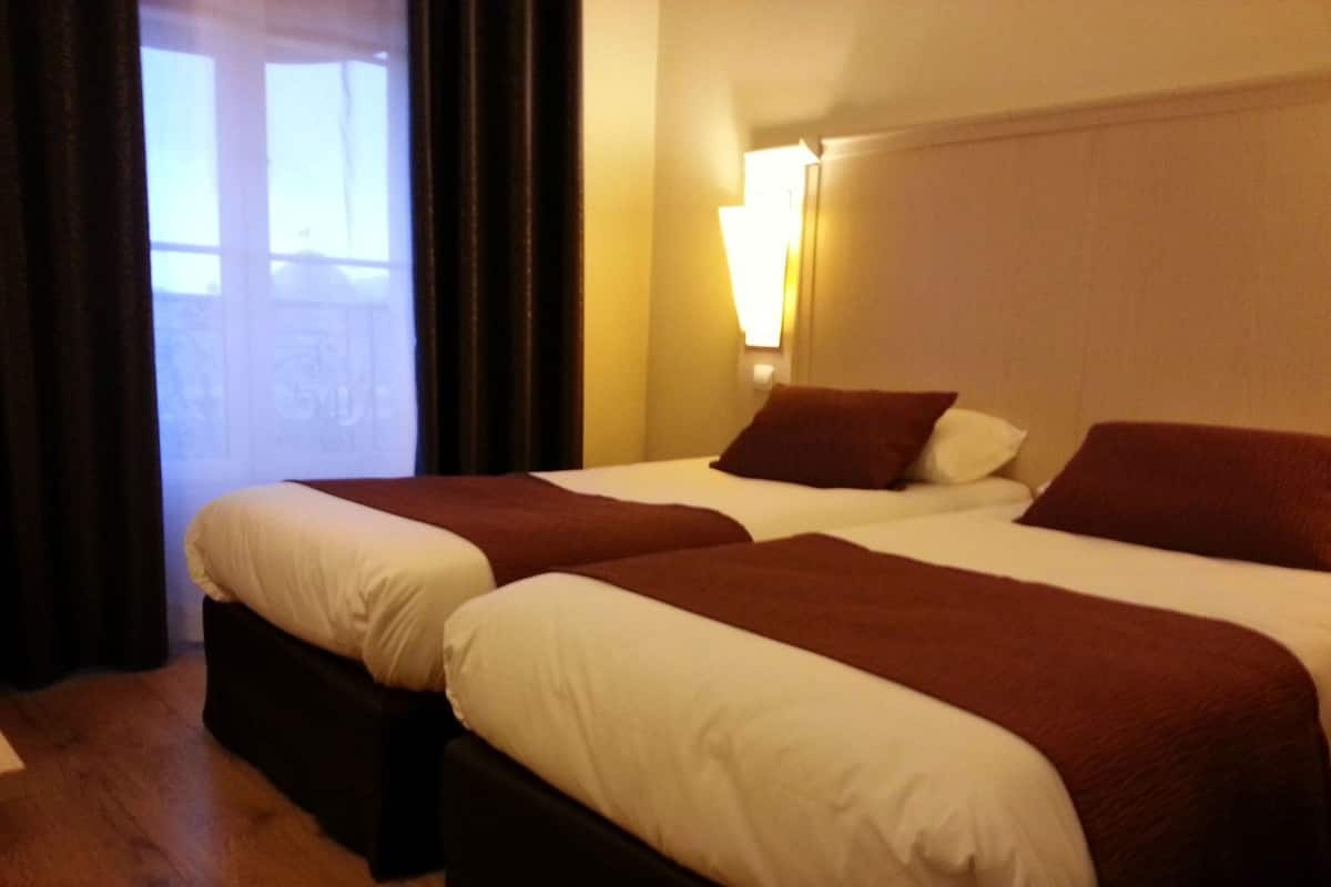 A hotel room with two beds, a window with curtains, and a wall-mounted lamp.