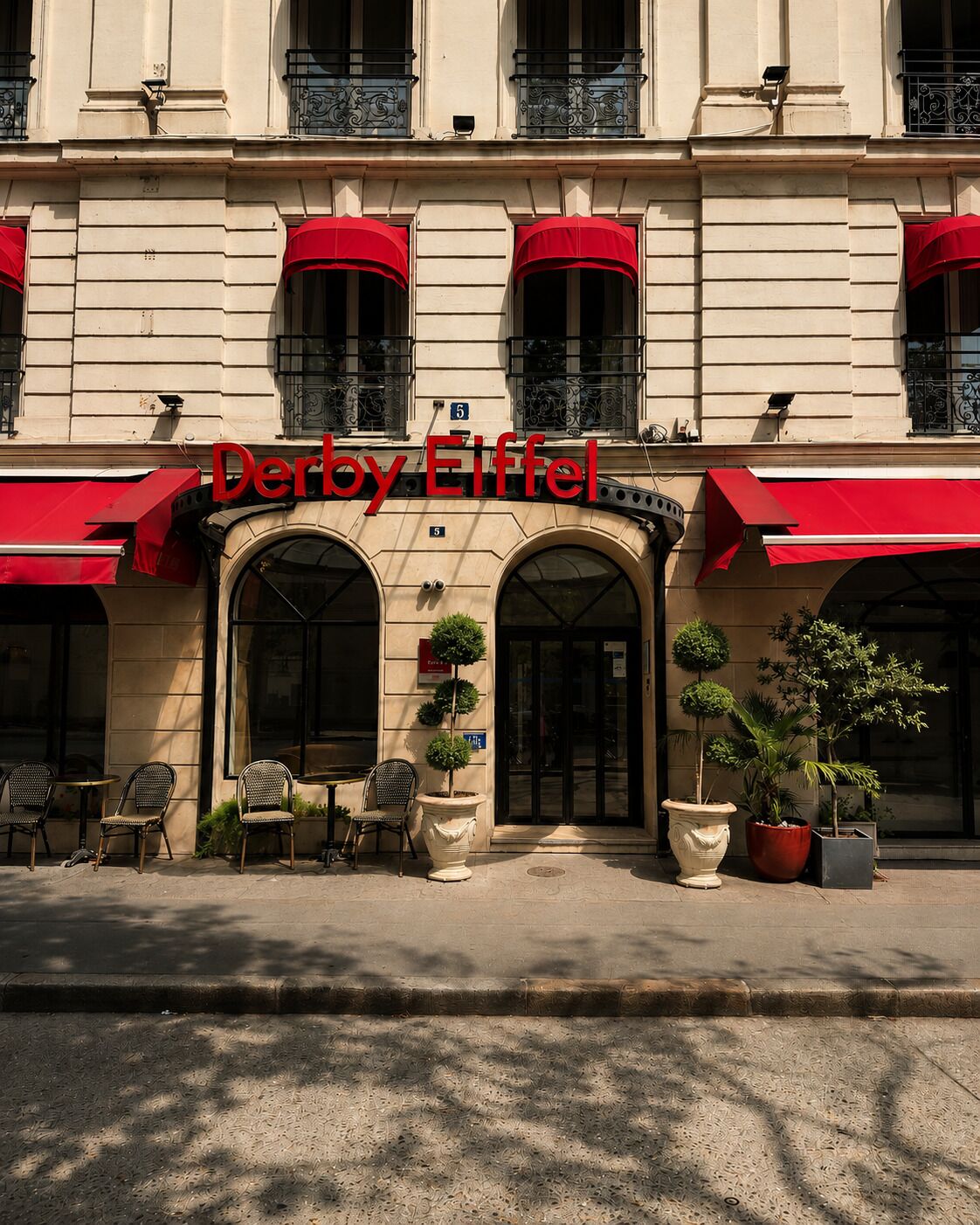 Un edificio con un letrero que dice 'Derby Eiffel' y el número '5' sobre la entrada. Cuenta con espacios al aire libre con sillas y mesas, y macetas con plantas ubicadas frente a la entrada.