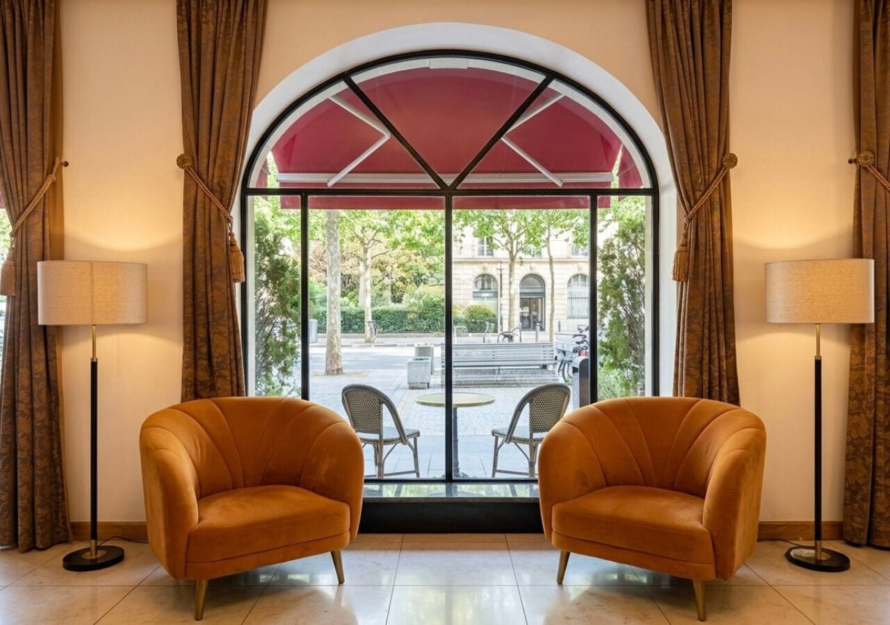 A room with two armchairs facing a large window with a view of a building and trees.
