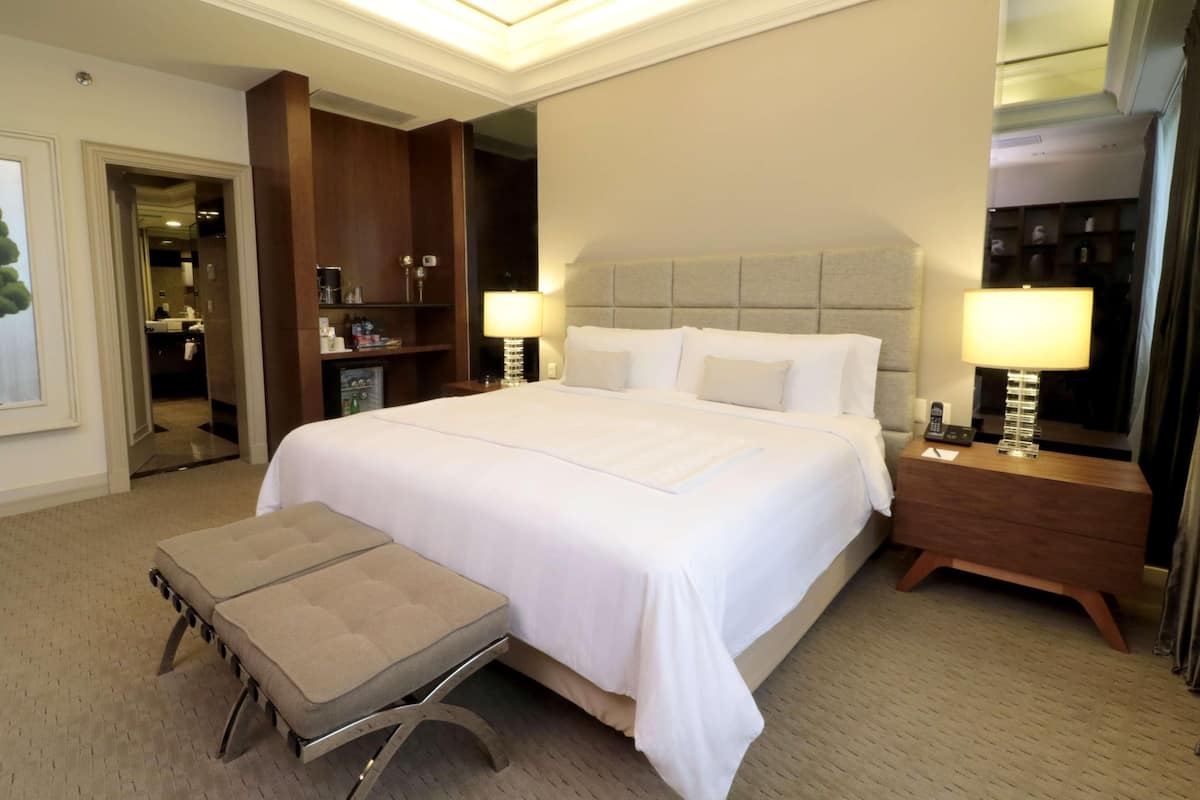 Quarto de hotel com uma cama grande, mesas de cabeceira, um banco e um guarda-roupa.