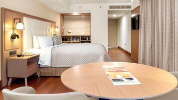 Habitación de hotel con cama, mesita de noche, lámpara y una mesa redonda con sillas.