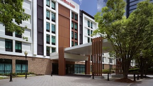 A modern building with a Hilton Garden Inn sign, featuring a mix of white and brown facades, large windows, and a covered entrance area with trees.