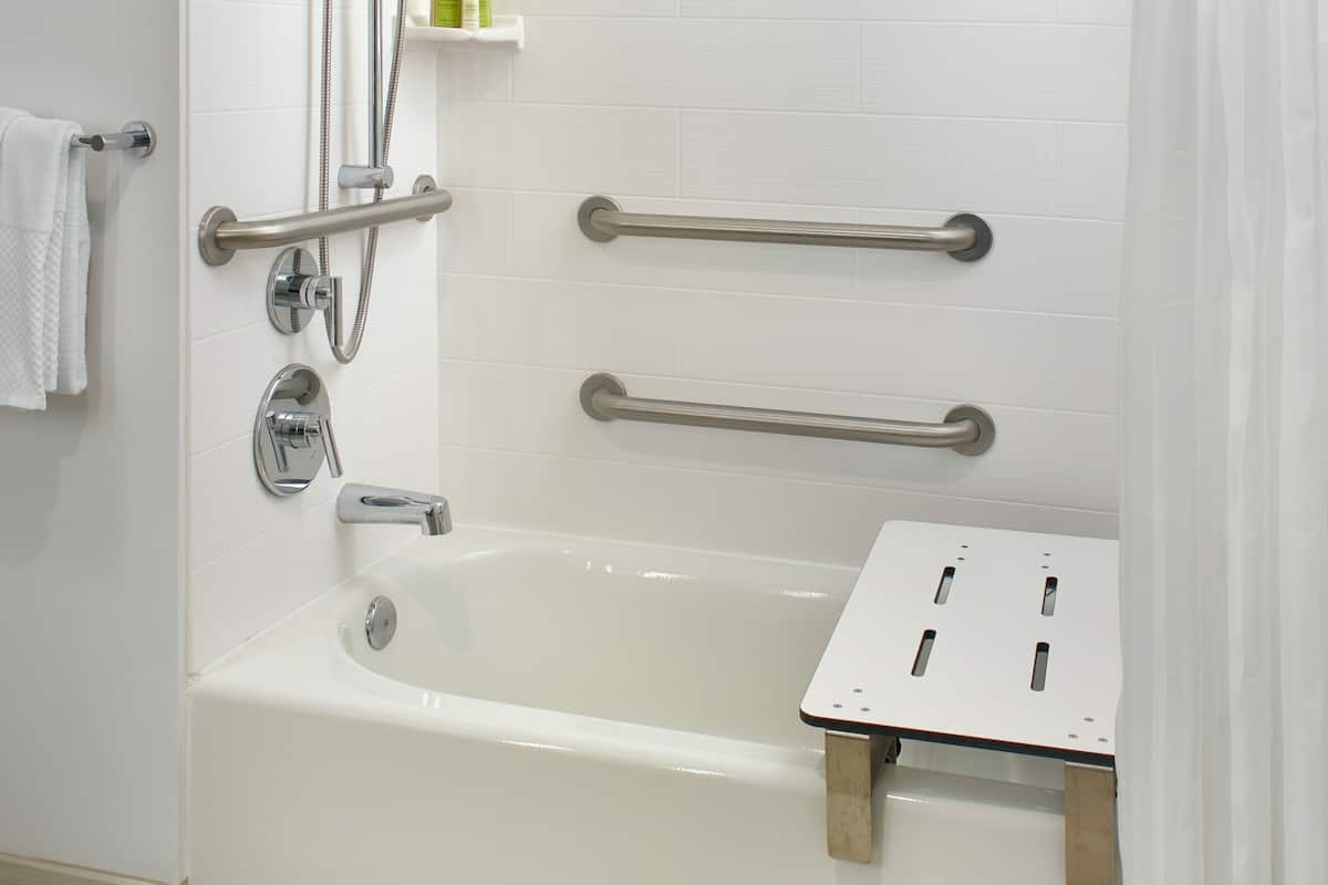 A modern bathroom with a bathtub, grab bars, and a shower head.