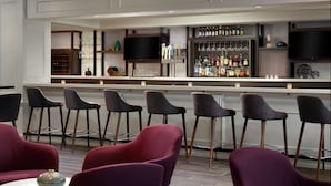 A bar area with multiple stools, a television, and a variety of bottles and glasses on shelves.