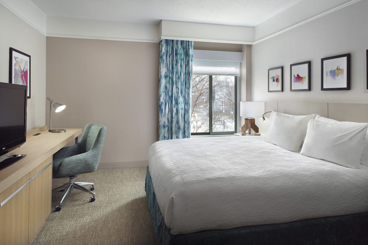 A hotel room with a bed, desk, chair, TV, and artwork on the walls.