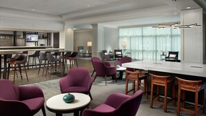 A modern hotel lobby with a bar area, seating arrangements, and a television screen.
