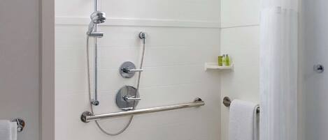A walk-in shower with a grab bar, a small table, and a towel rack.