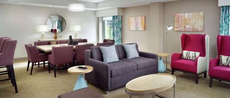 Una habitación de hotel moderna con comedor, un conjunto de sofás y un ventanal grande.