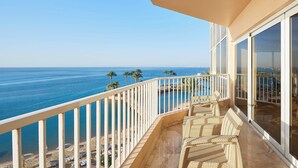 A balcony with wicker furniture overlooking a beach and ocean.