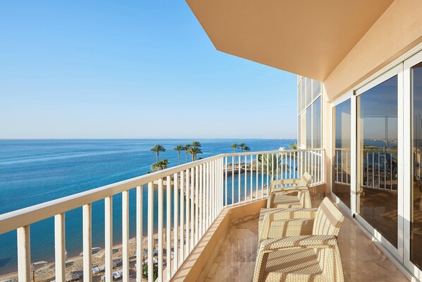 A balcony with wicker furniture overlooking a beach and ocean.