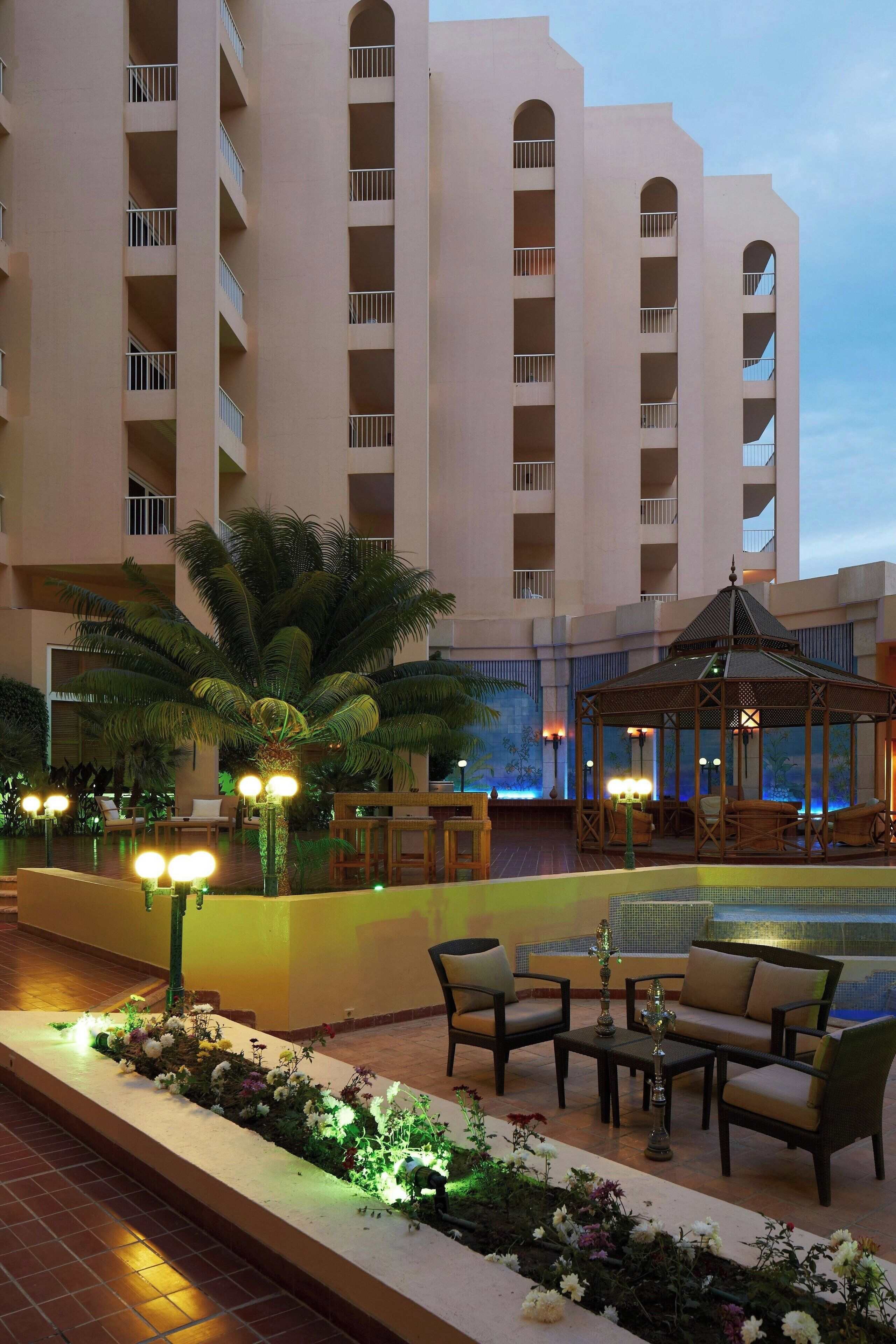 A hotel lobby with a pool, outdoor seating, and a large building in the background.
