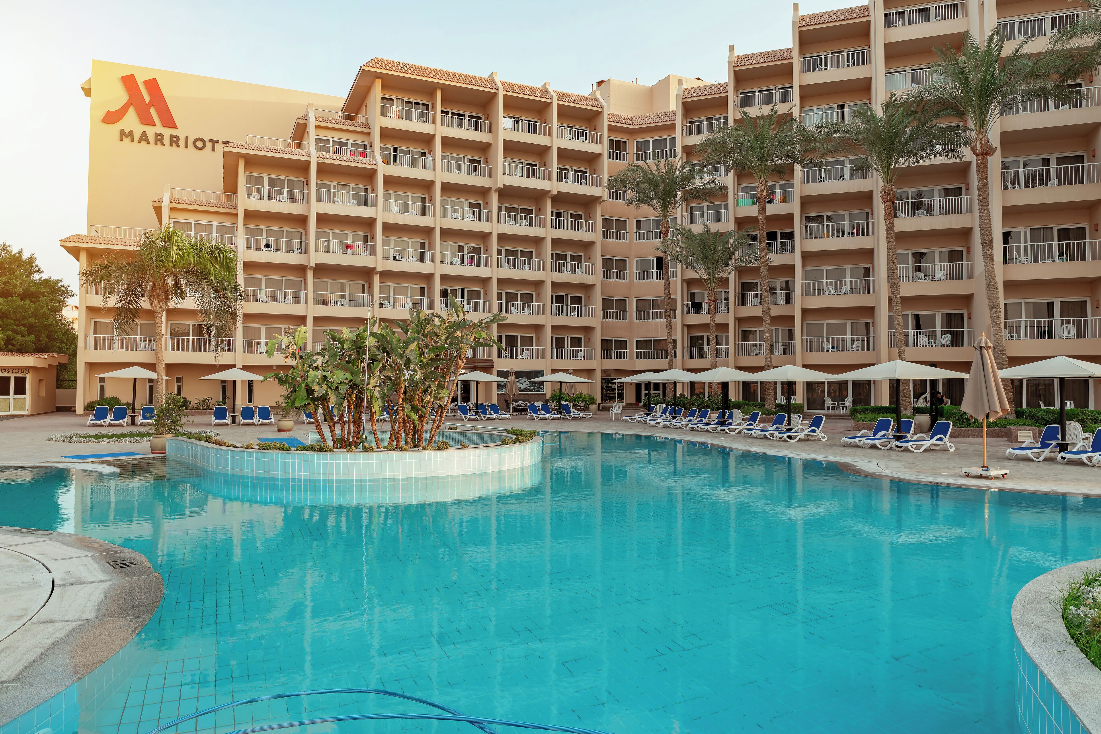 Un hotel Marriott con piscina rodeada de sillones de descanso y palmeras.