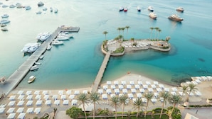 A marina with boats docked, a beach with sun loungers, and a small island with palm trees.