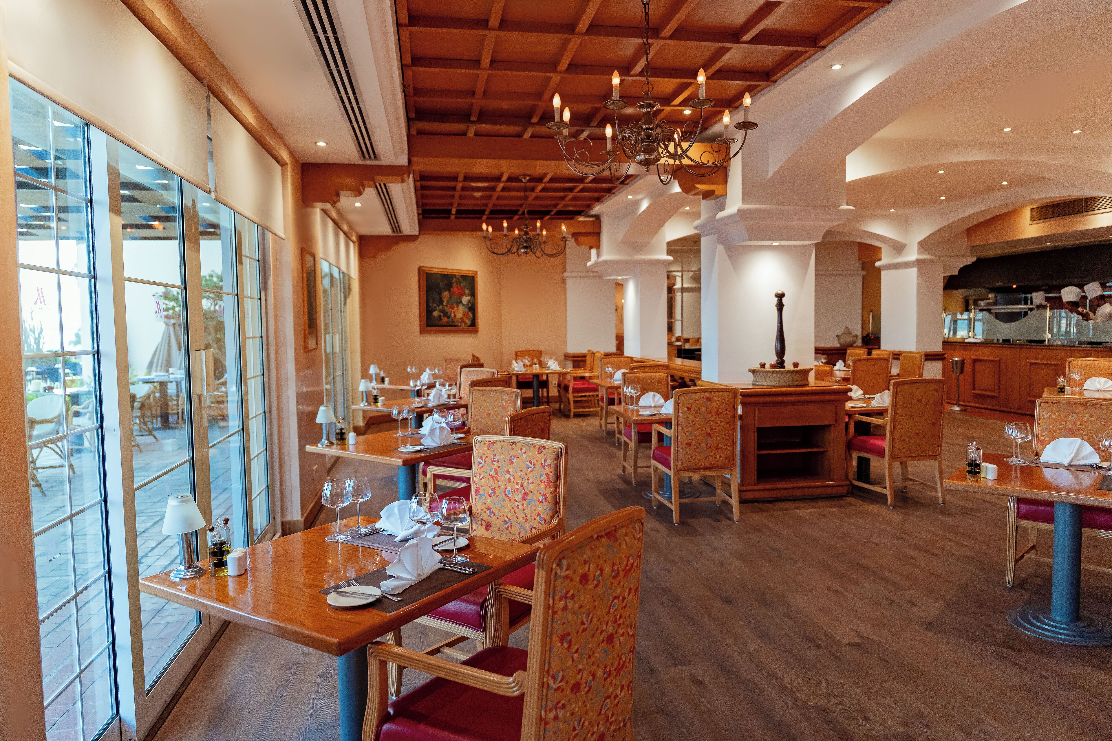 A restaurant with wooden tables and chairs, large windows, and a chandelier.