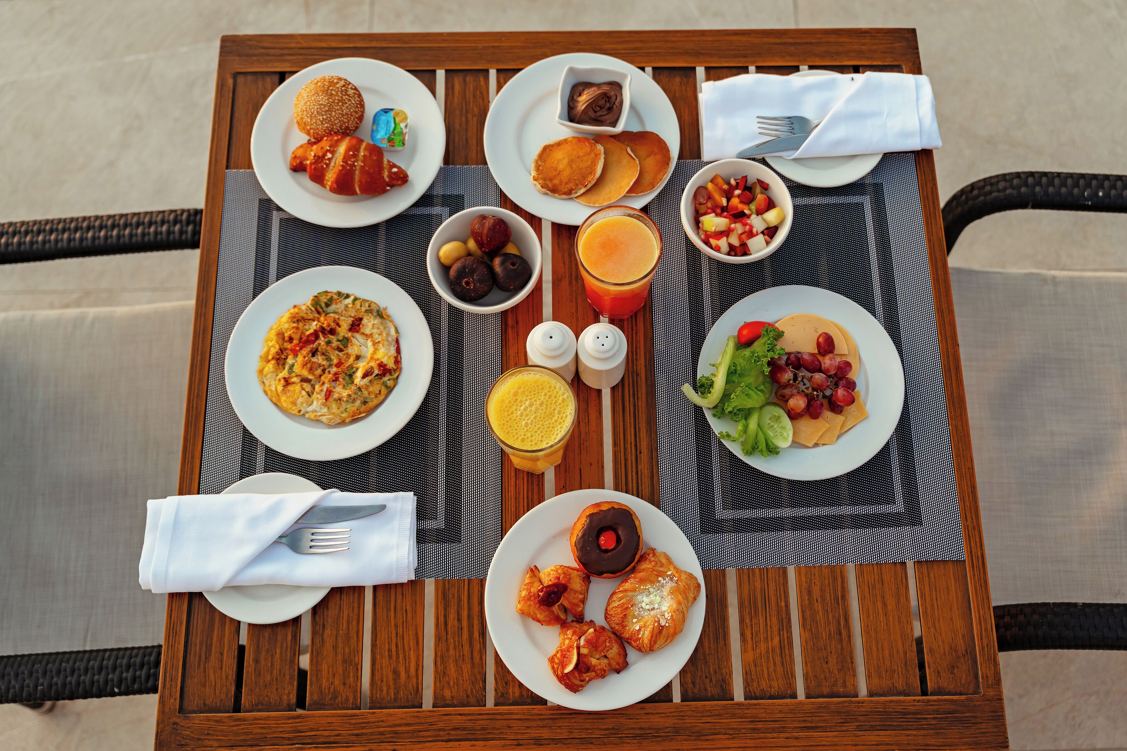 A breakfast table with plates of food, a glass of juice, and condiments.