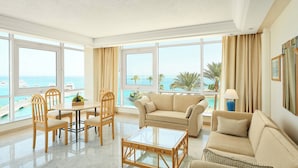 A spacious living room with a large window overlooking a pool and the sea, featuring a sofa, chairs, and a coffee table.