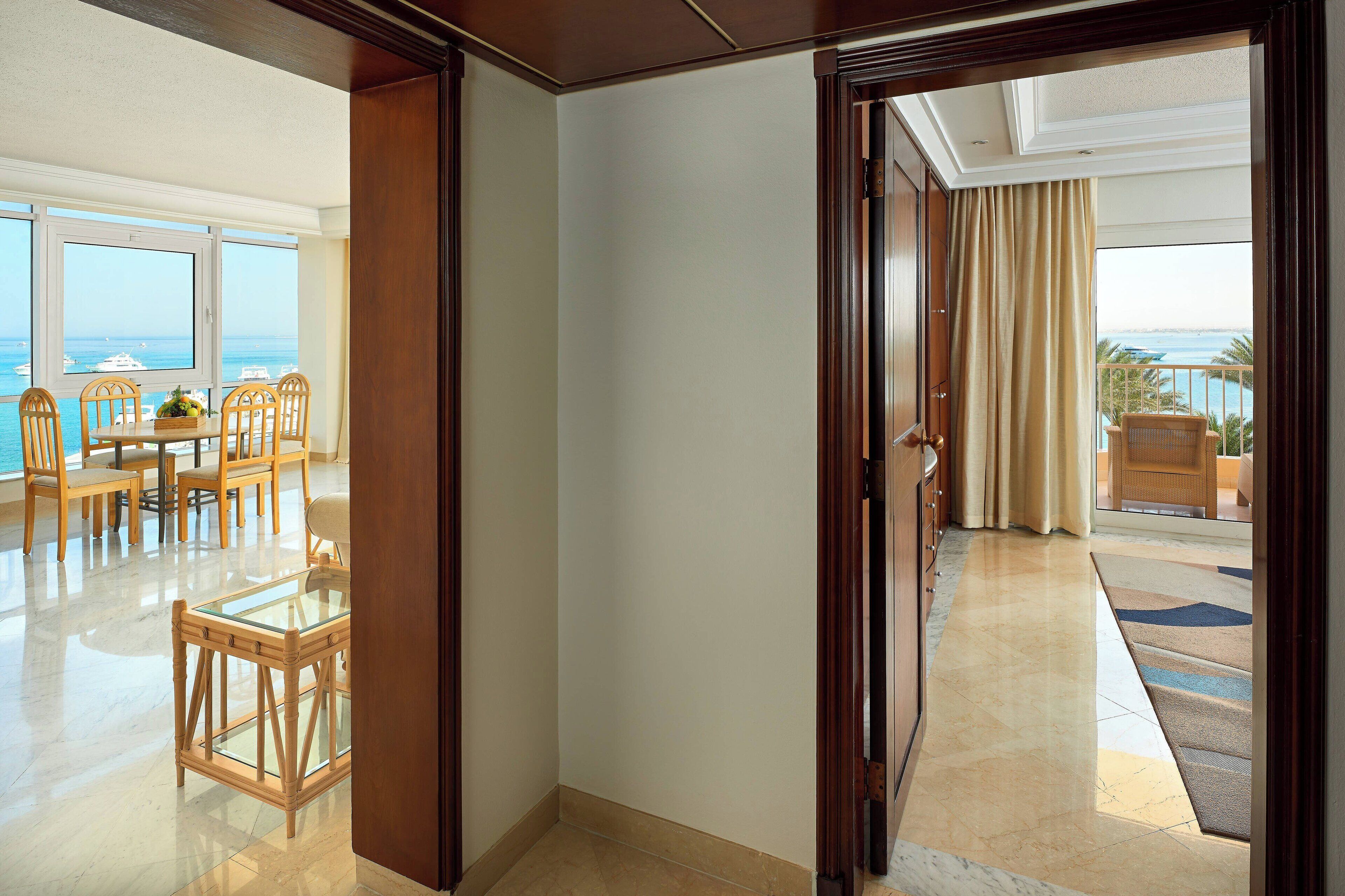 A hotel room with a view of the ocean, a dining area with wooden furniture, and a balcony with a view of the sea.