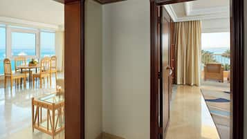 A hotel room with a view of the ocean, a dining area with wooden furniture, and a balcony with a view of the sea.