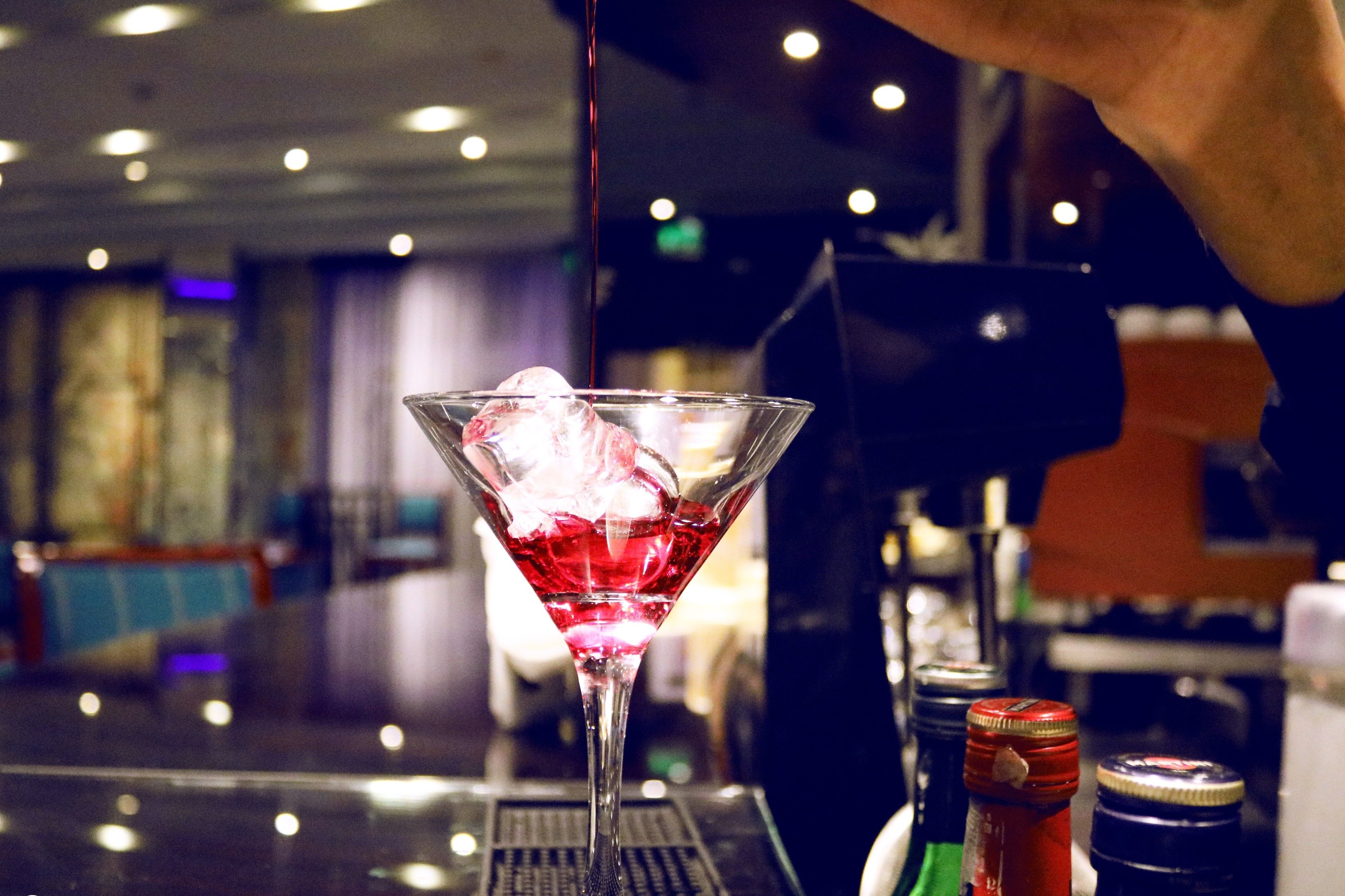 A martini glass with a red drink and ice cubes on a bar counter.