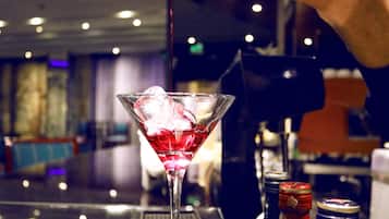 A martini glass with a red drink and ice cubes on a bar counter.