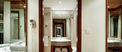 Une salle de bain d’hôtel avec un lavabo doté d’un plan de travail en granit, un miroir et un sèche-cheveux fixé au mur.
