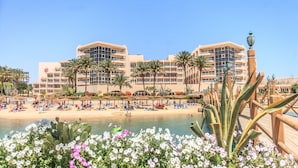 A hotel with multiple floors, a pool, and a beach area with sun loungers.
