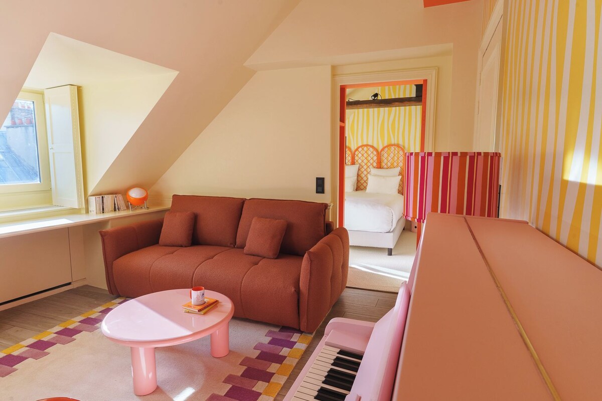 A cozy room with a brown sofa, a pink table, and a piano.