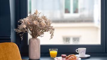 Una mesa para el desayuno con un jarrón de flores secas, un vaso de zumo de naranja, un croissant y una taza de café en un alféizar.