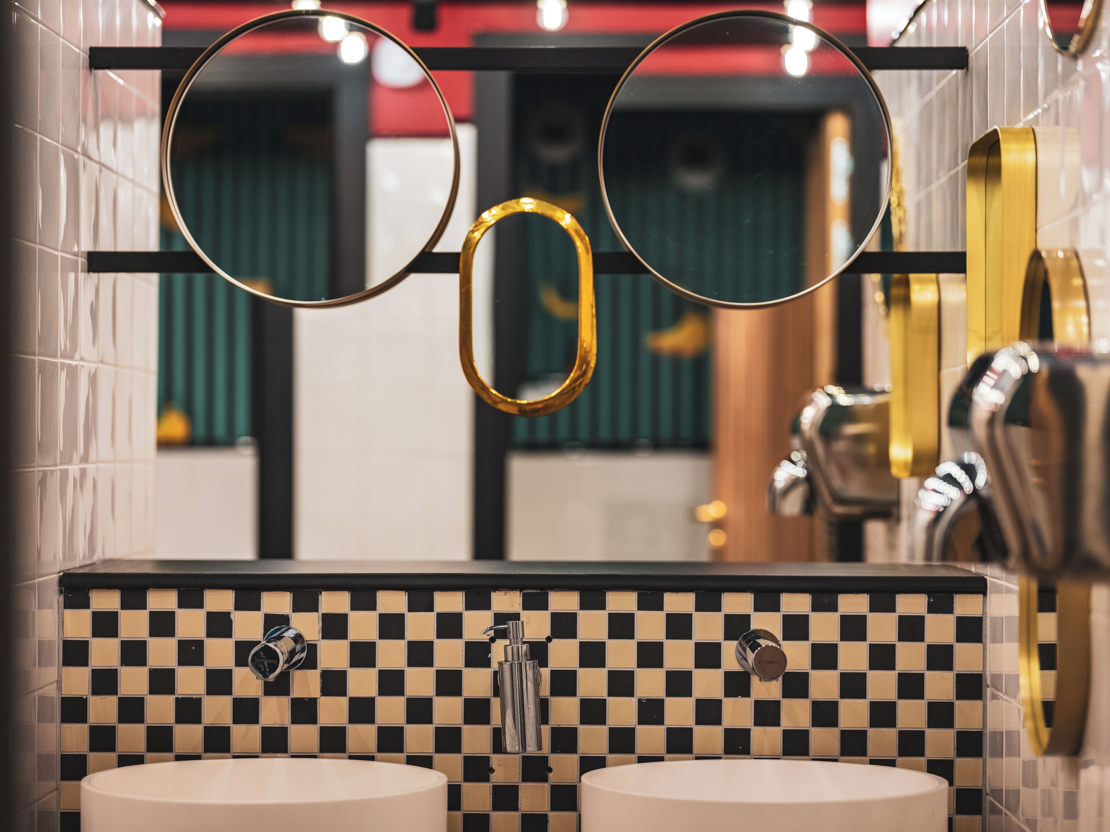 Une salle de bain avec deux lavabos, un dosseret carrelé à motifs et un miroir avec un cadre doré.