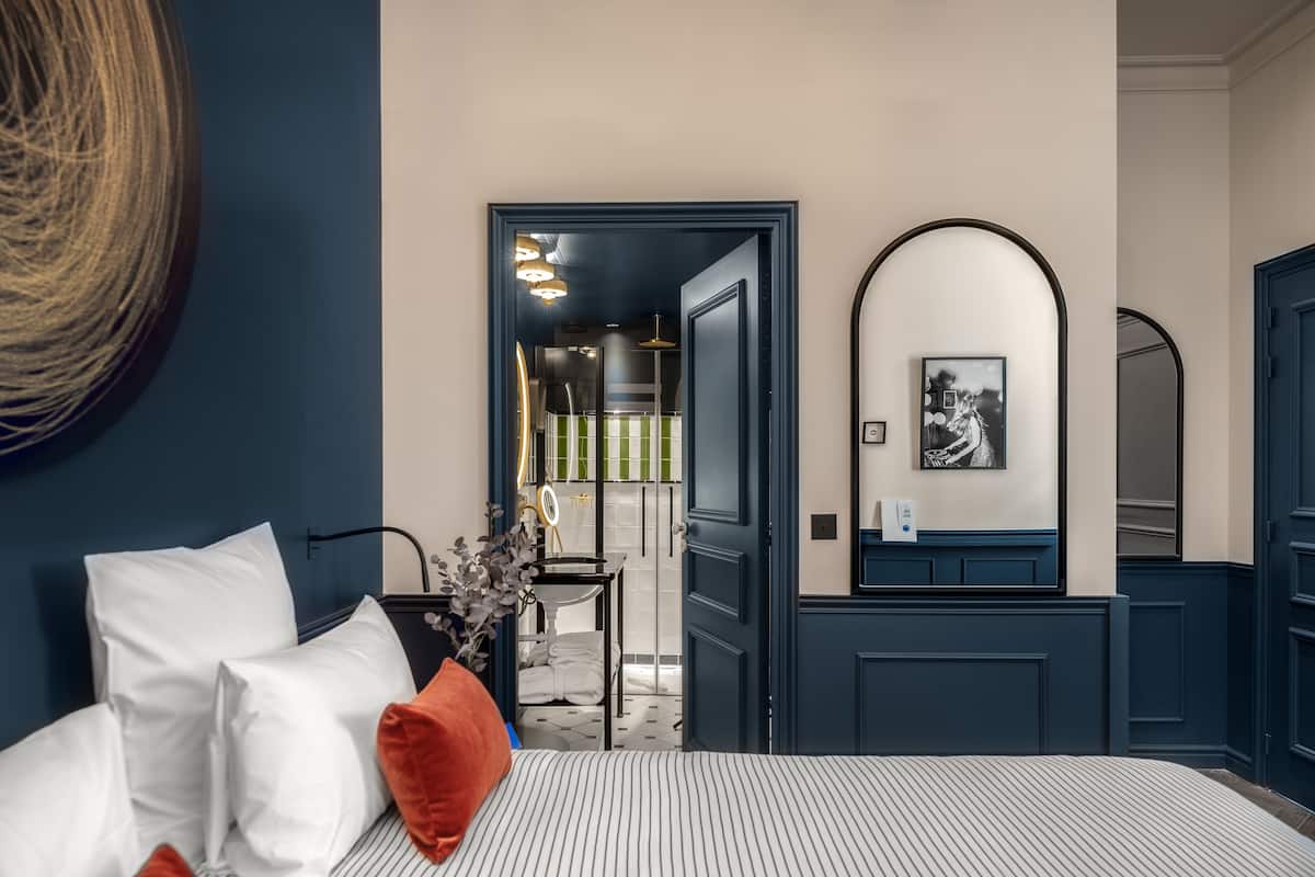 Una habitación de hotel con cama, espejo, puerta y vista al baño.