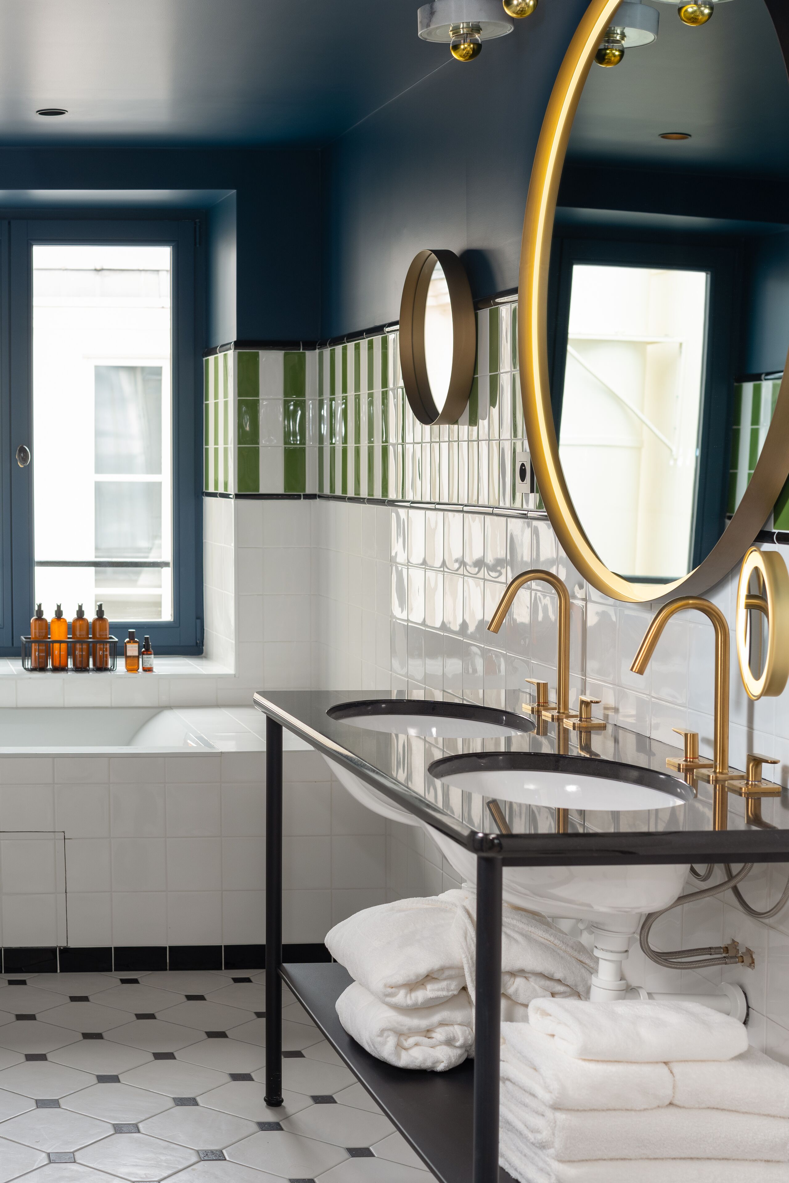 Un baño moderno con una bañera grande, dos lavamanos con detalles dorados y un espejo amplio.