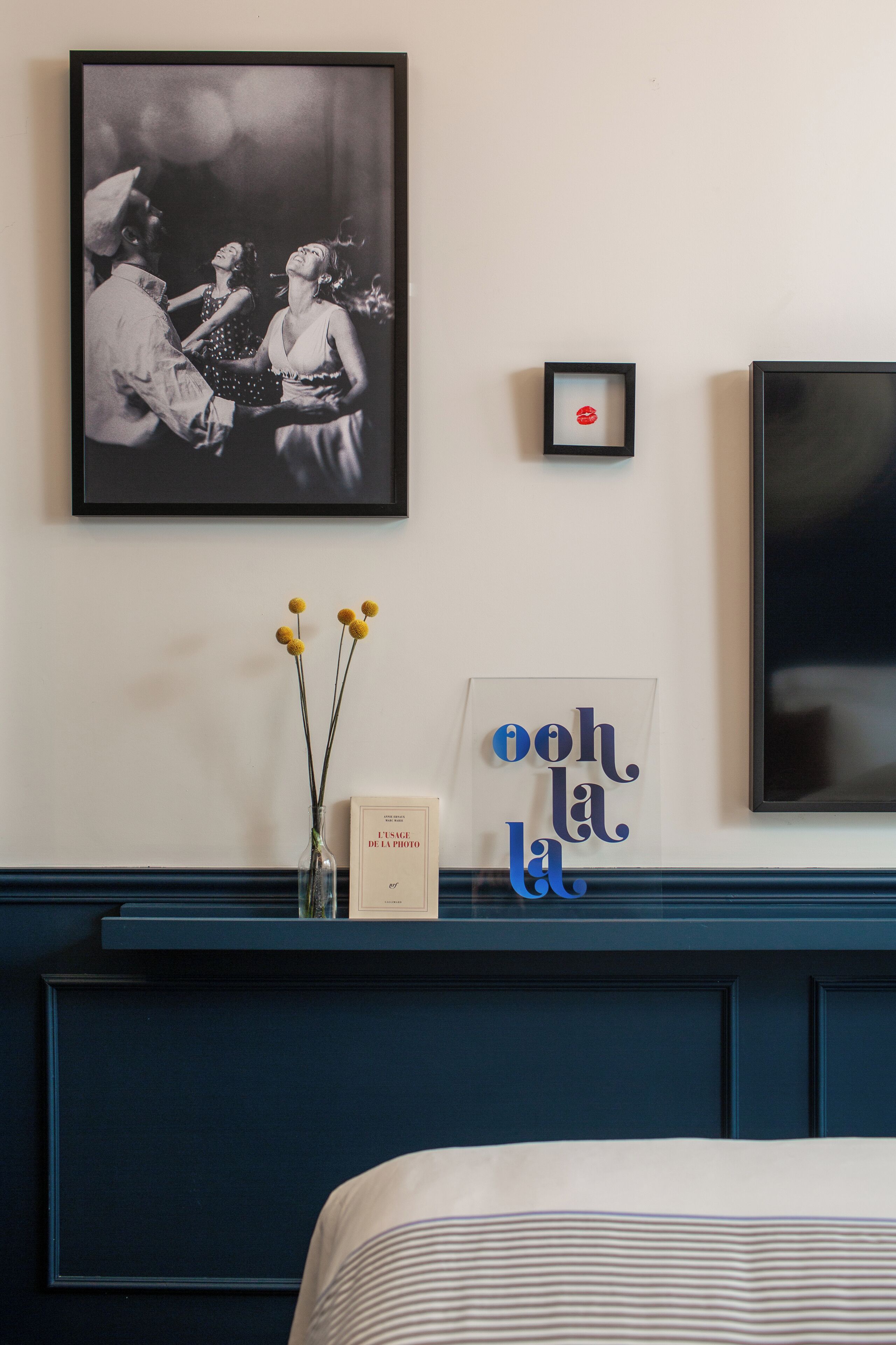 Un dormitorio con una cama, una fotografía en blanco y negro enmarcada, un cuadro pequeño enmarcado y un letrero decorativo.