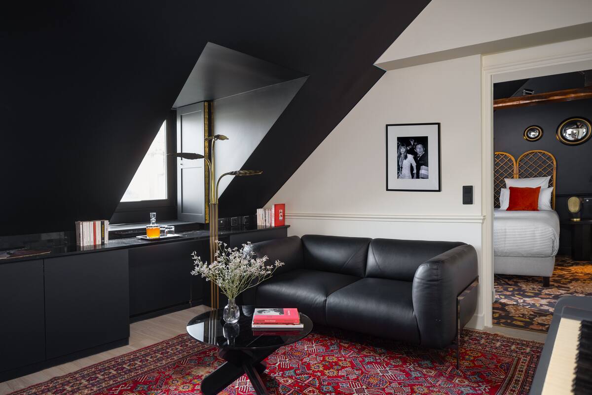 Una sala de estar moderna con un sofá de cuero negro, una mesa de centro de vidrio y un tapete rojo estampado.