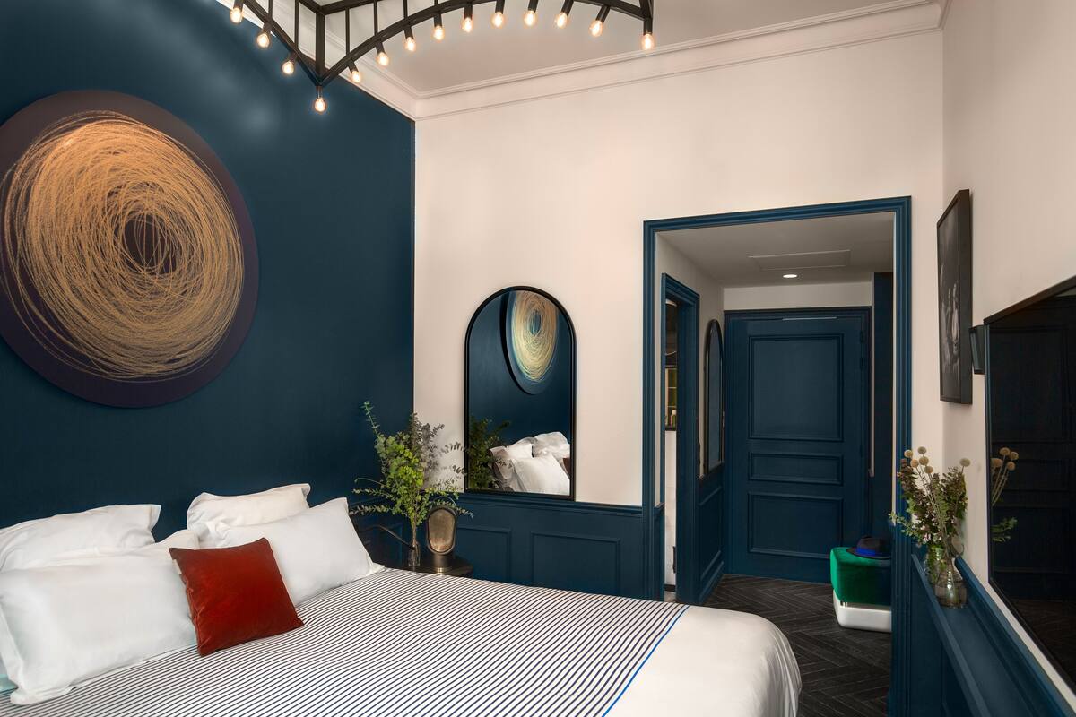 Una habitación de hotel moderna con una cama grande, un espejo y una pared de acento azul oscuro.