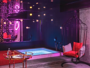 Une salle de spa moderne équipée d’un jacuzzi, d’un fauteuil suspendu et d’une petite table avec une bouteille.