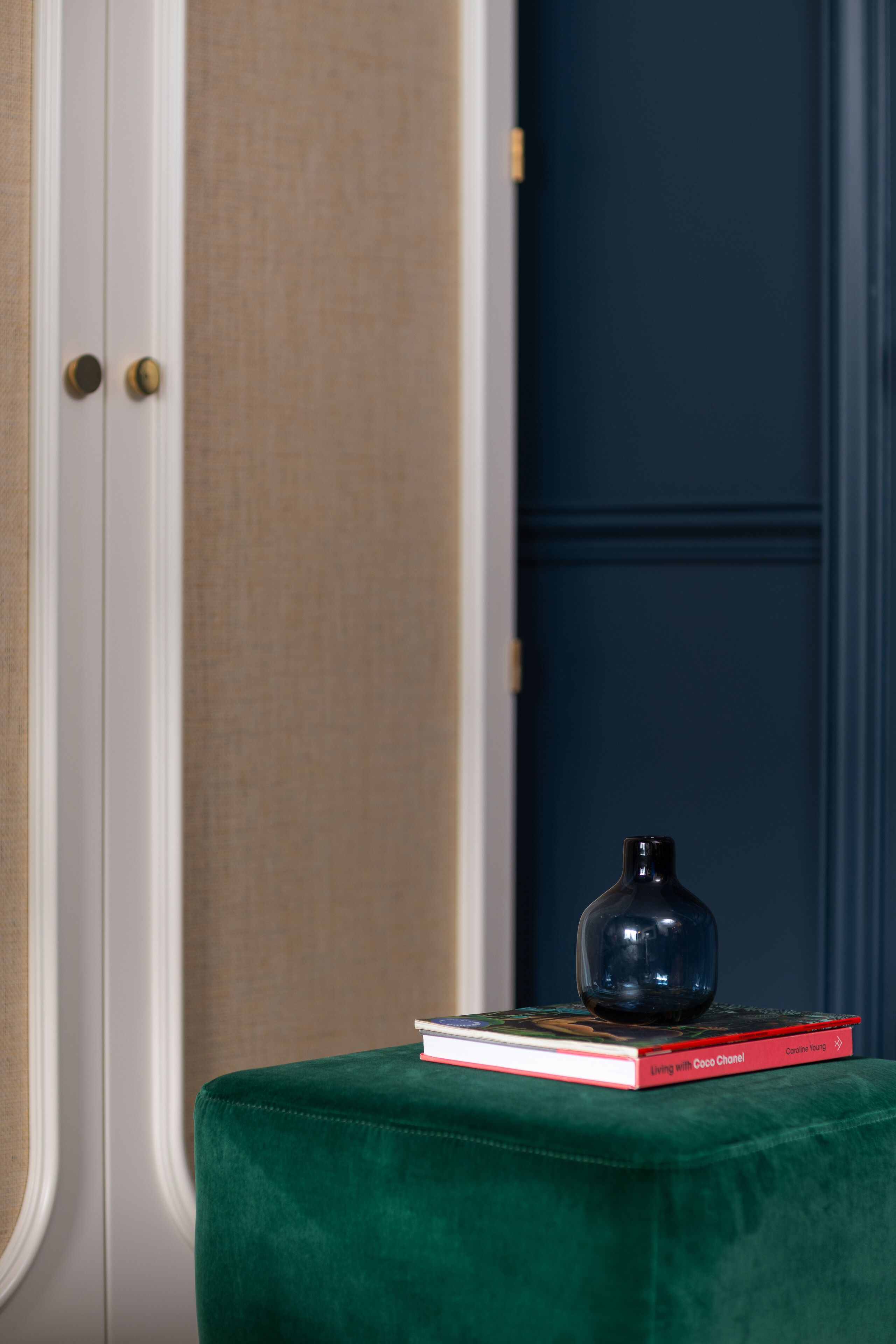 A green ottoman with a book and a black vase on top.
