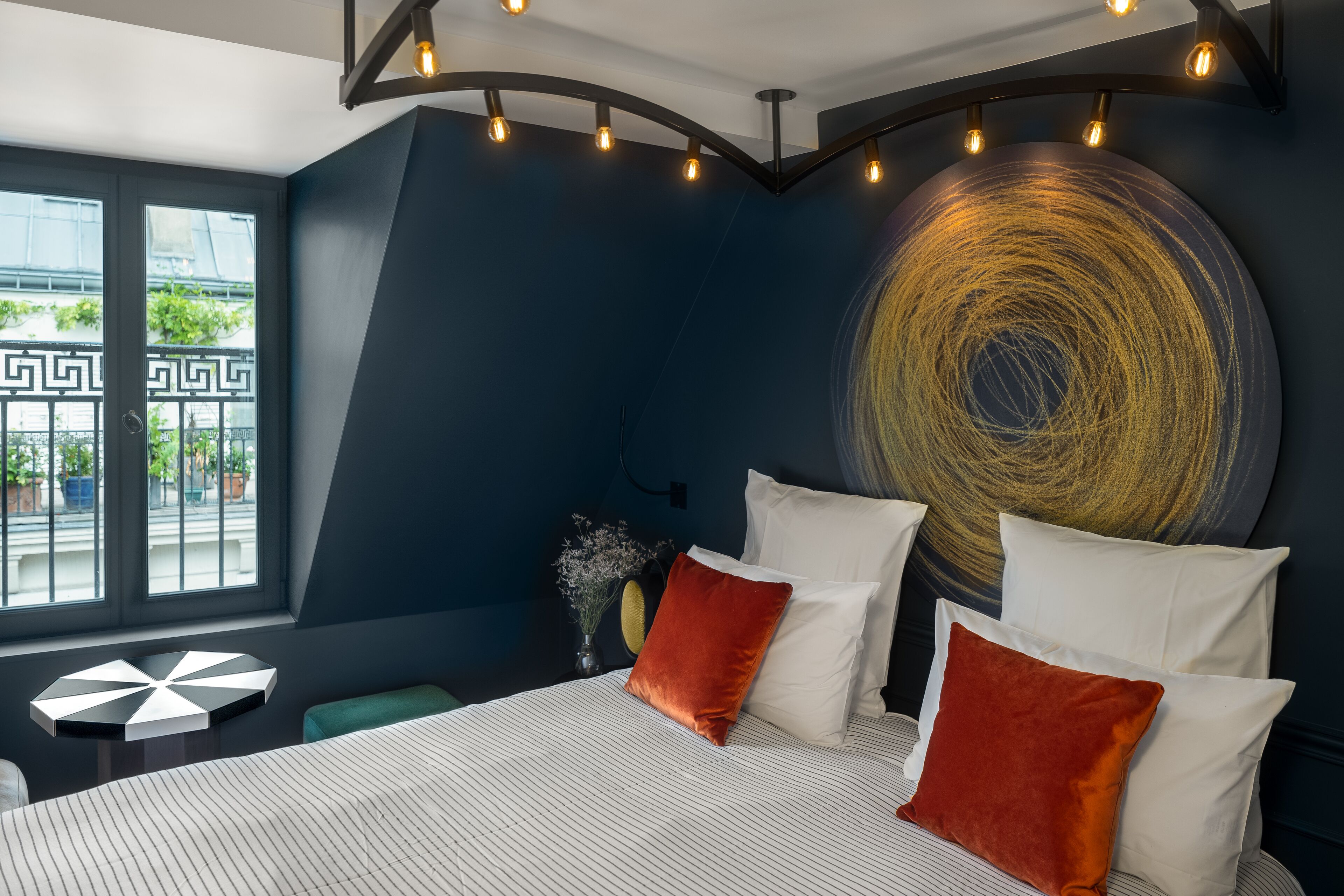 A modern bedroom with a large bed, a unique wall art piece, and a geometric floor lamp.