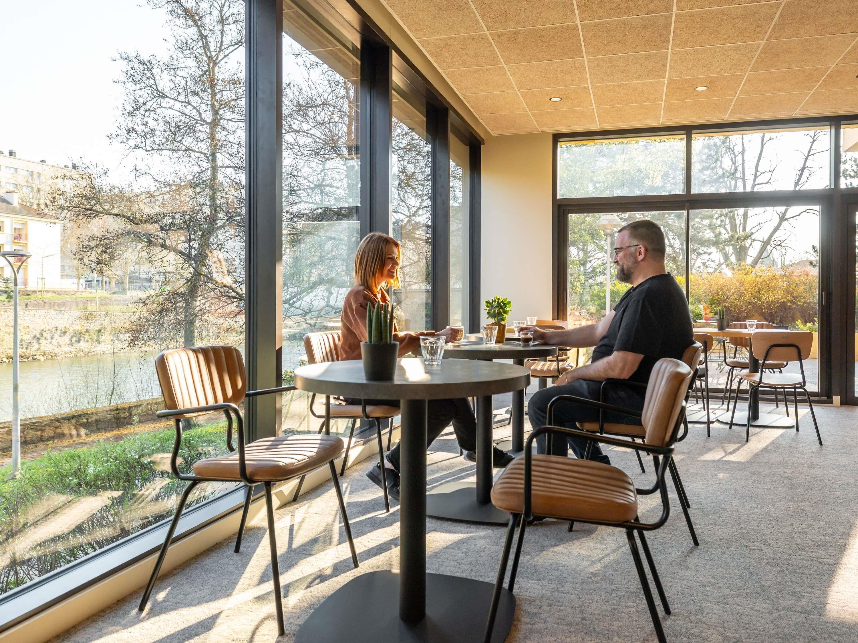 A cafe with large windows, a view of a river, and outdoor seating.