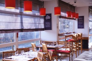 Enjoy dining in a spacious restaurant with large windows offering views of the outside, wooden tables, and pendant lights.