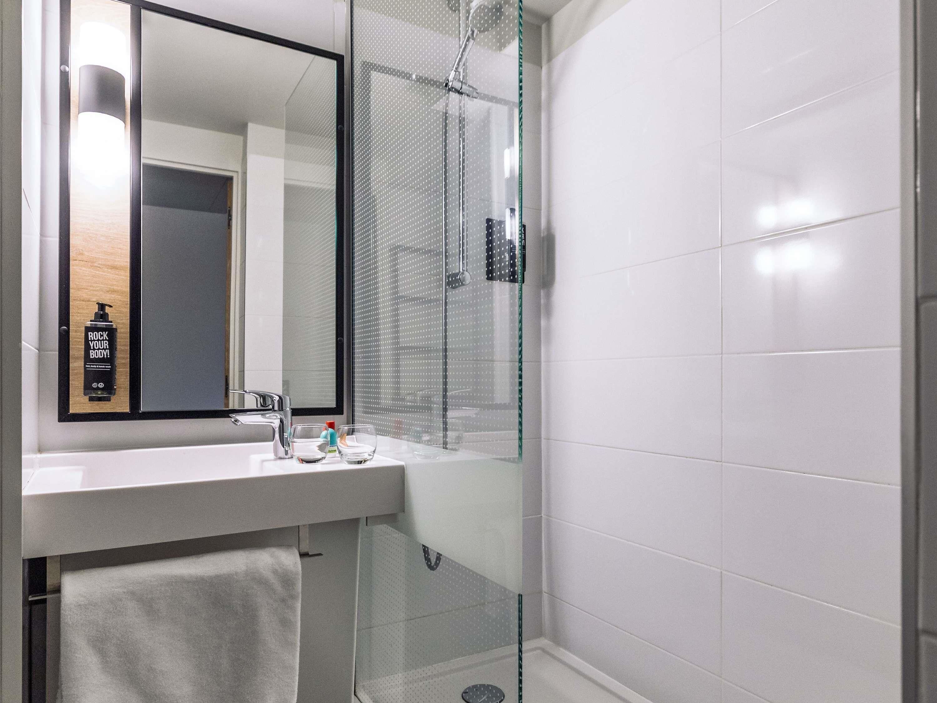 A modern bathroom with a glass shower enclosure, a large mirror, and a white sink.