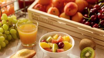 A breakfast setting with a bowl of fruit, a glass of orange juice, and a crate of peaches.